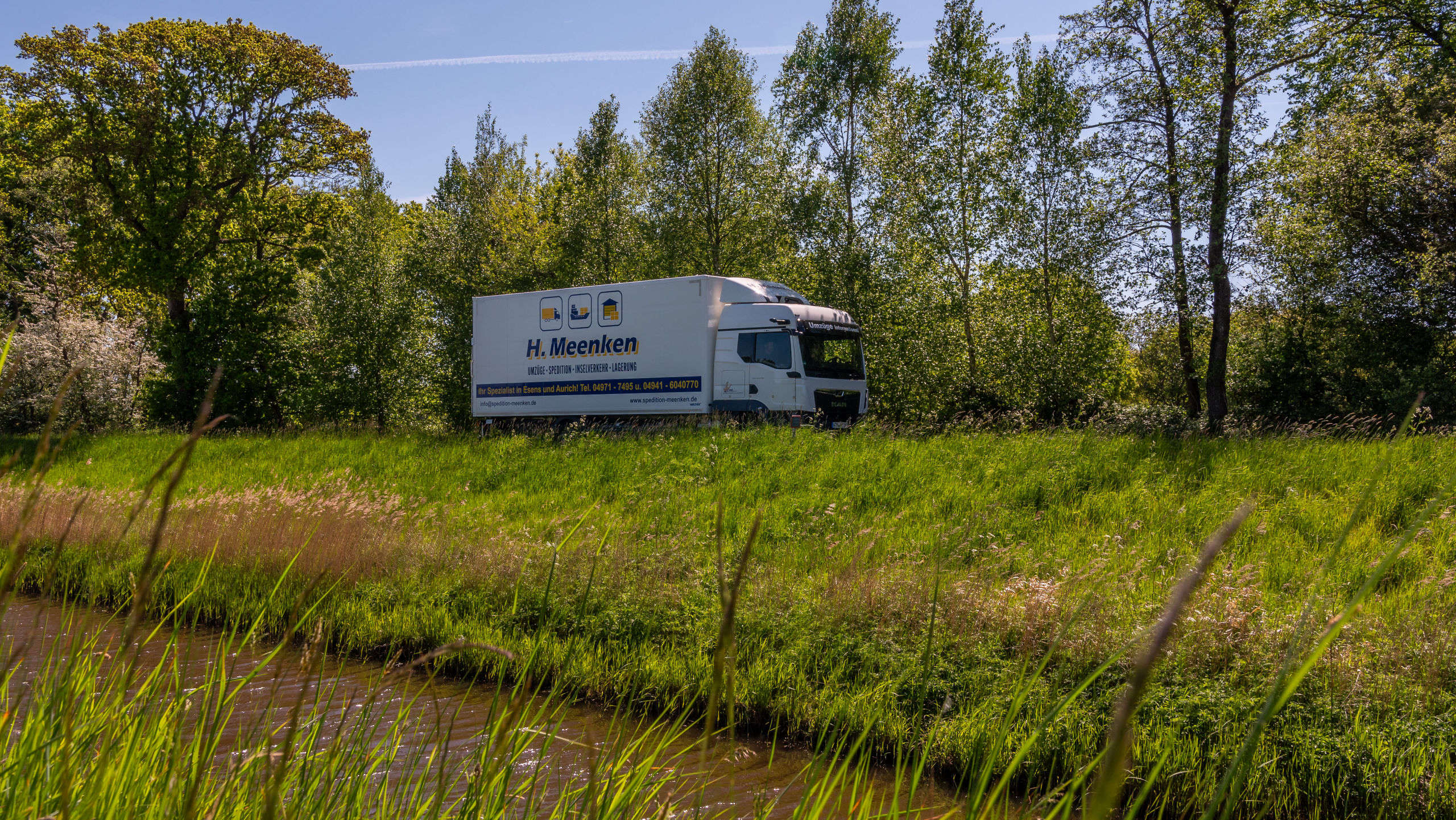 LKW der Spedition fährt auf einer Landstraße am Kanal entlang