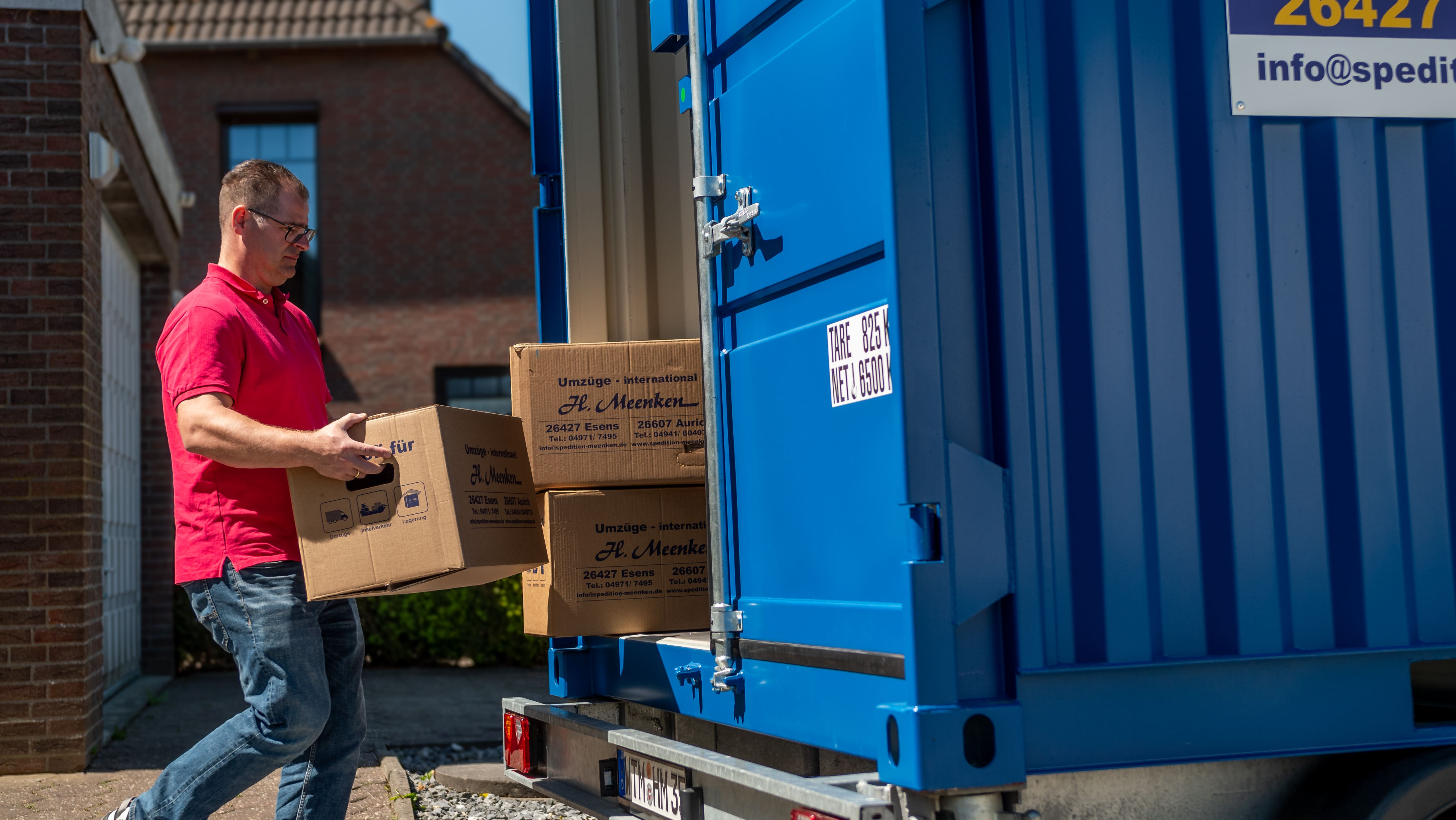 Mitarbeiter räumt Kartons in einen blauen Seecontainer