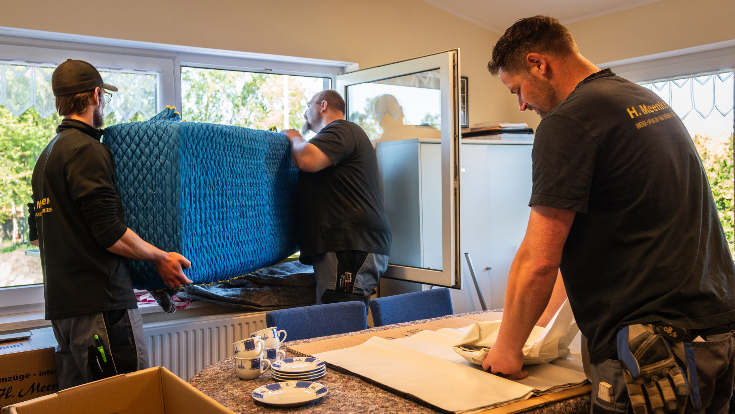 Drei Mitarbeiter die ein Möbelstück aus dem Fenster heben